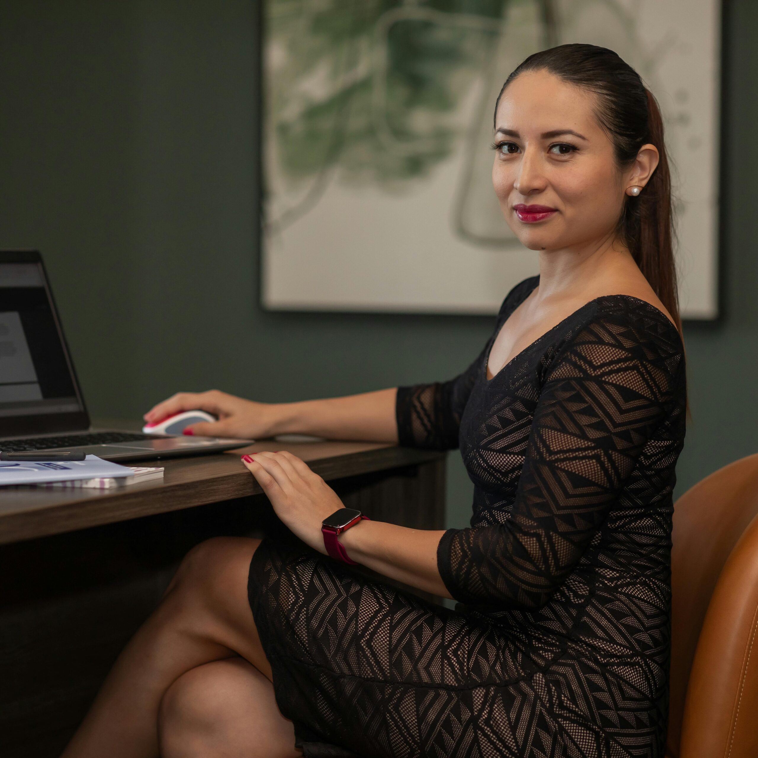 Confident businesswoman in stylish dress working on a laptop at her desk.